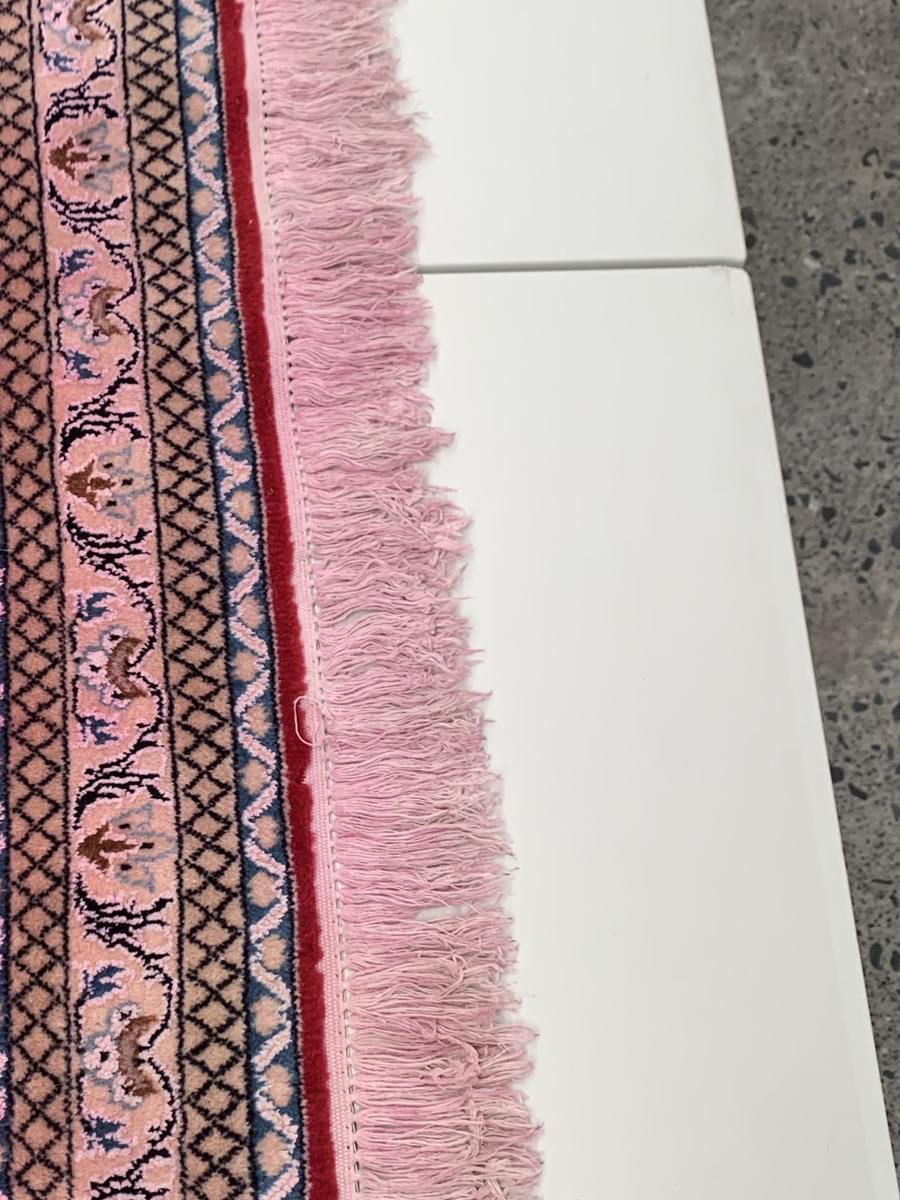 The cotton fringe of a red Persian rug stained pink, where dye from the wool has bled into it