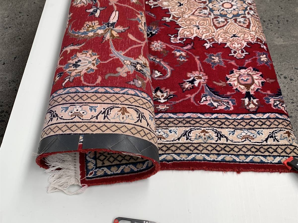 A red Persian rug rolled on a bench for fringe and edge finishing
