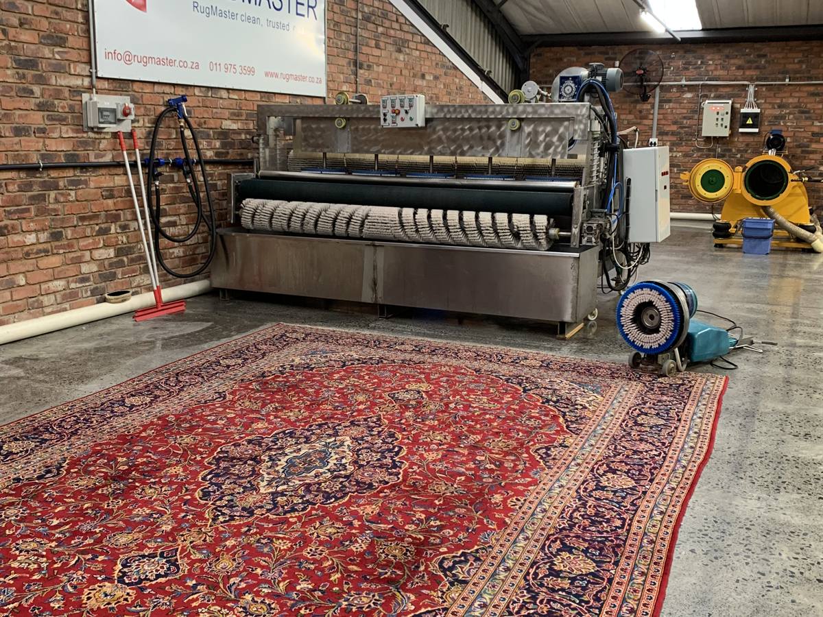 A washed Persian rug laid out on the plant floor in front of the wash machine