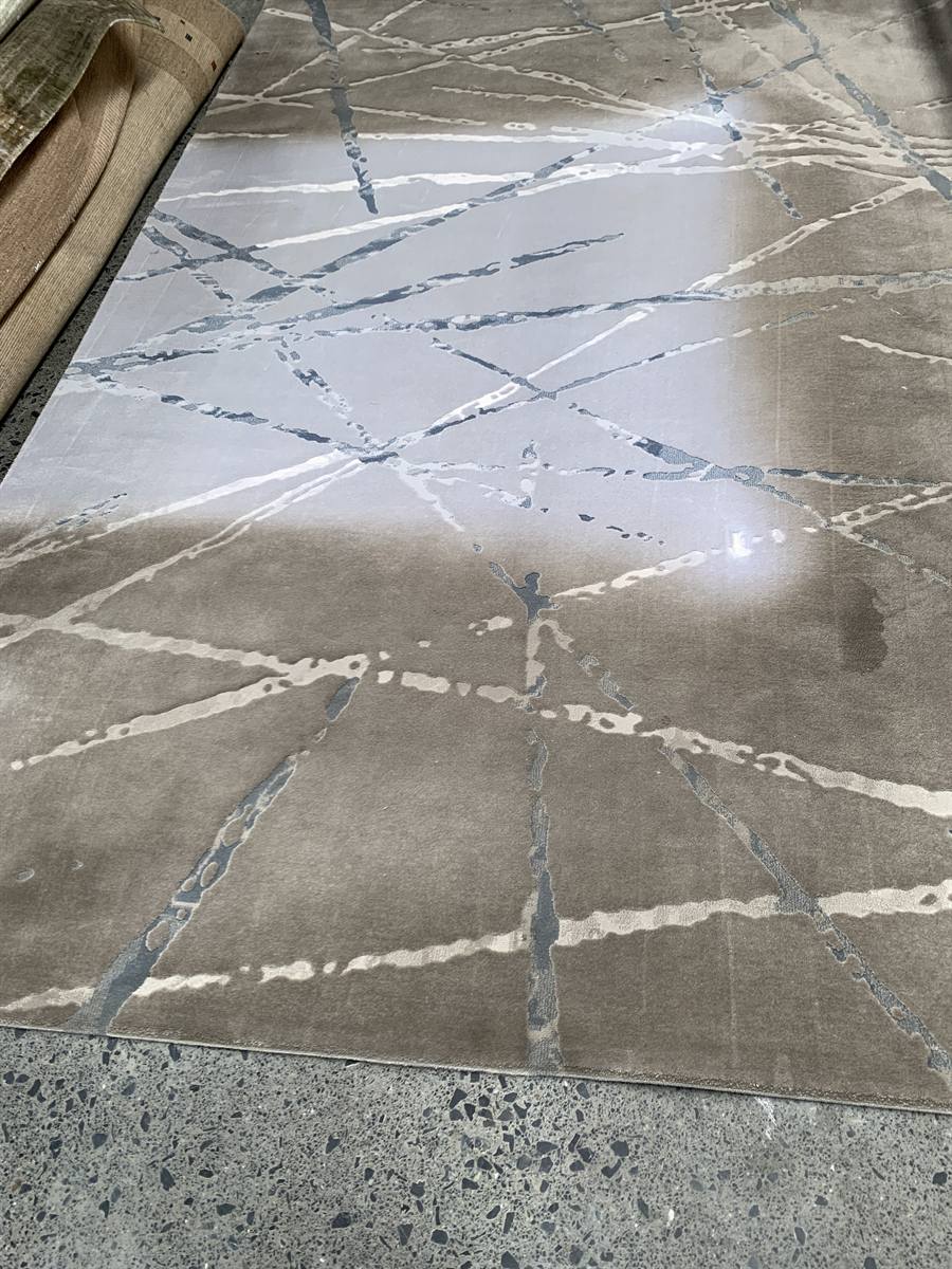 A silver and grey patterned rug before cleaning, the ground dulled to a flat brown by years of settled soil