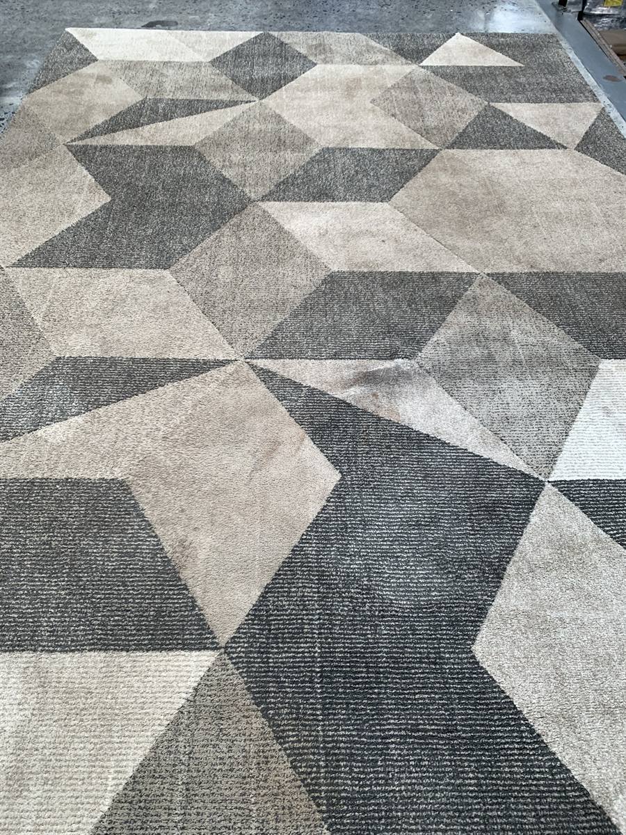 A grey geometric wool rug before washing, the pattern flattened and greyed by a film of soil