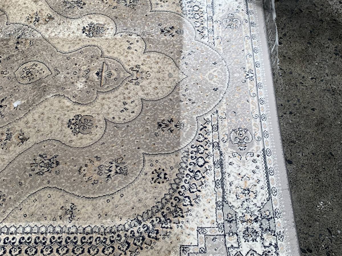 A cream and grey medallion rug part-way through washing, the cleaned section bright white against the dull beige of the section still to be done